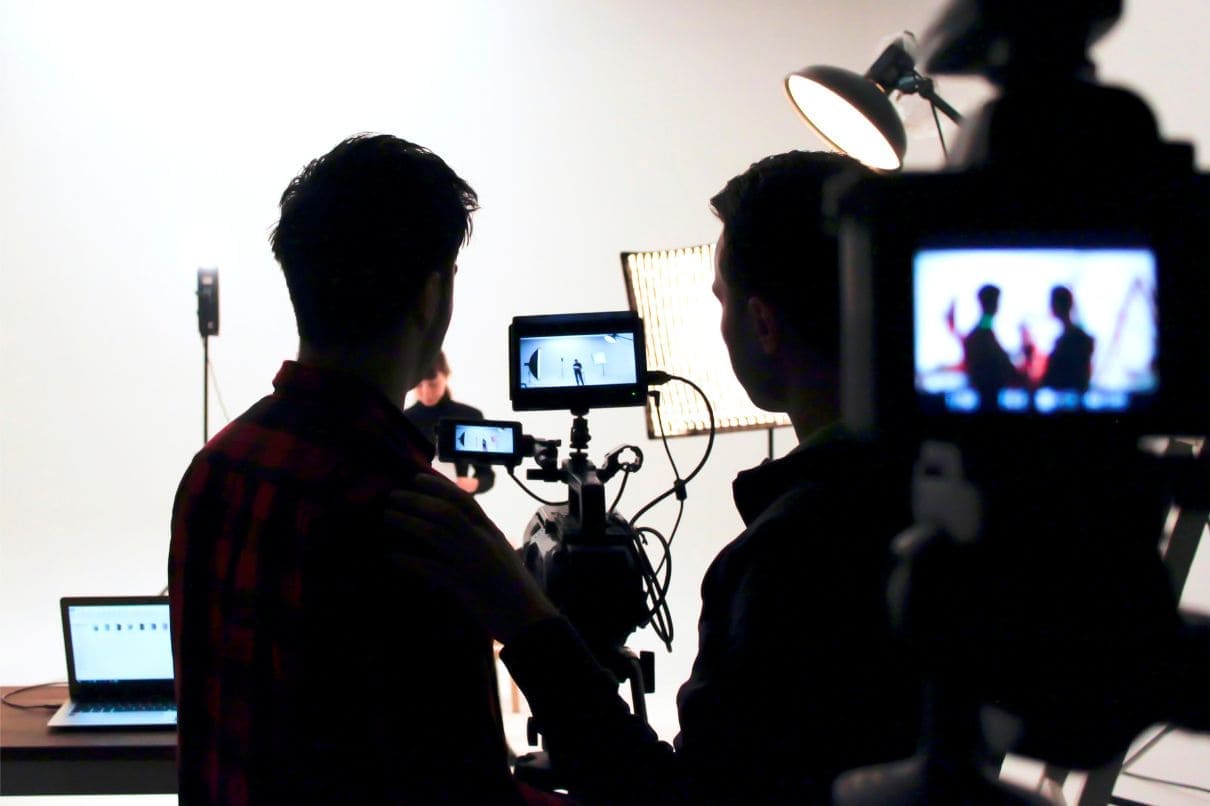Two men filming in a studio with a laptop, capturing moments on camera for a project.